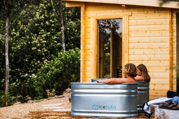 Maydena Wilderness Wellness at Maydena Bike Park couple sitting in cold plunge ice bath next to wooden sauna at maydena bike park new wellness centre in amongst dense rainforest
