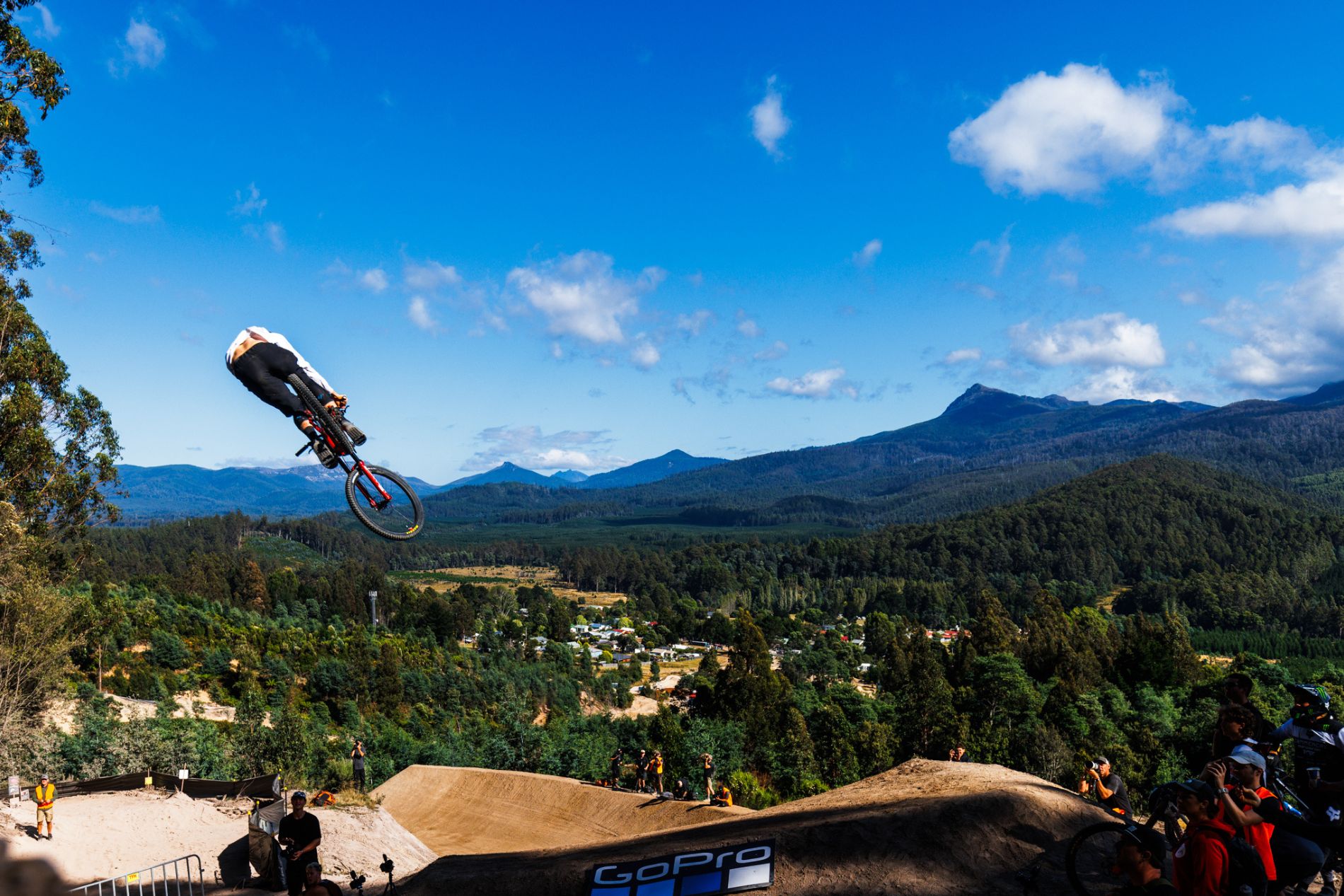 Bike jumping off big dirt jump with mountains and forest in Maydena in backdrop